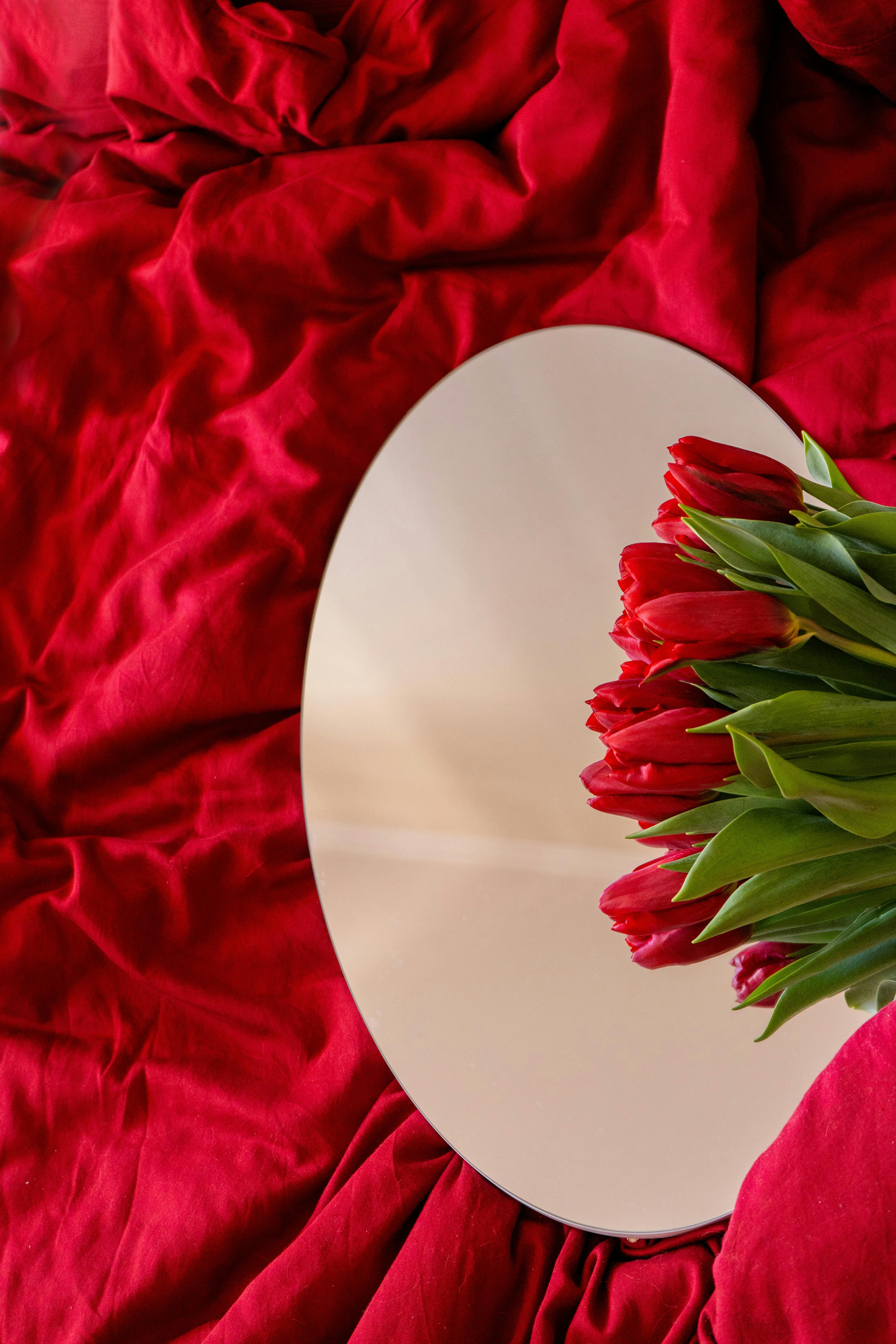 Red tulips reflected in a mirror create a romantic Valentine's Day composition on red fabric.
