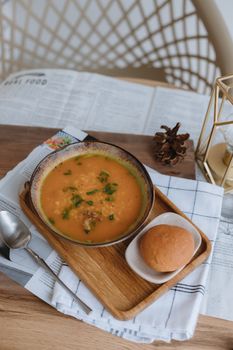 Warm and hearty pumpkin soup served with a bun on a tray, perfect for cozy indoor dining.
