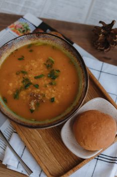 Warm bowl of tomato soup served with a fresh bread roll on a wooden tray, perfect for a cozy meal.