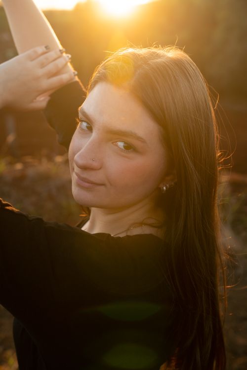 Free Portrait of a young woman smiling and posing outdoors in warm sunlight. Stock Photo