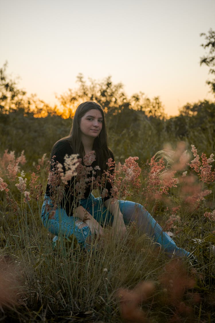 Woman Sitting On Meadow At Sunset