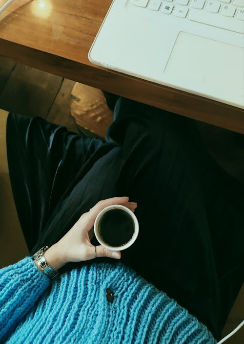 Woman Sitting at a Table with a Laptop and Holding a Coffee