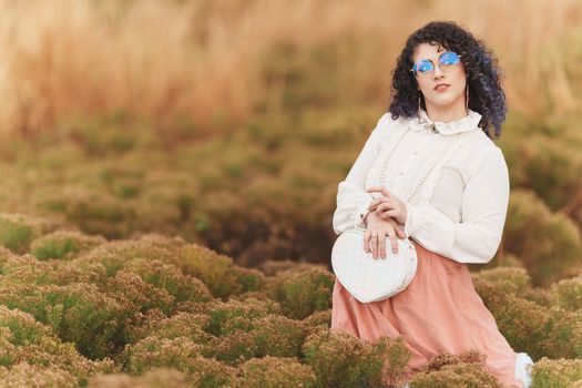 Fashionable woman posing in Kissimmee, FL field with heart-shaped purse and stylish blouse.