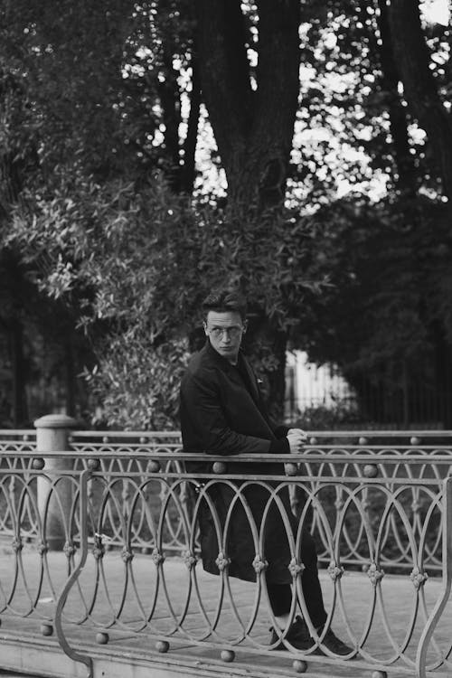 Grayscale Photo of Man Leaning on Metal Railing