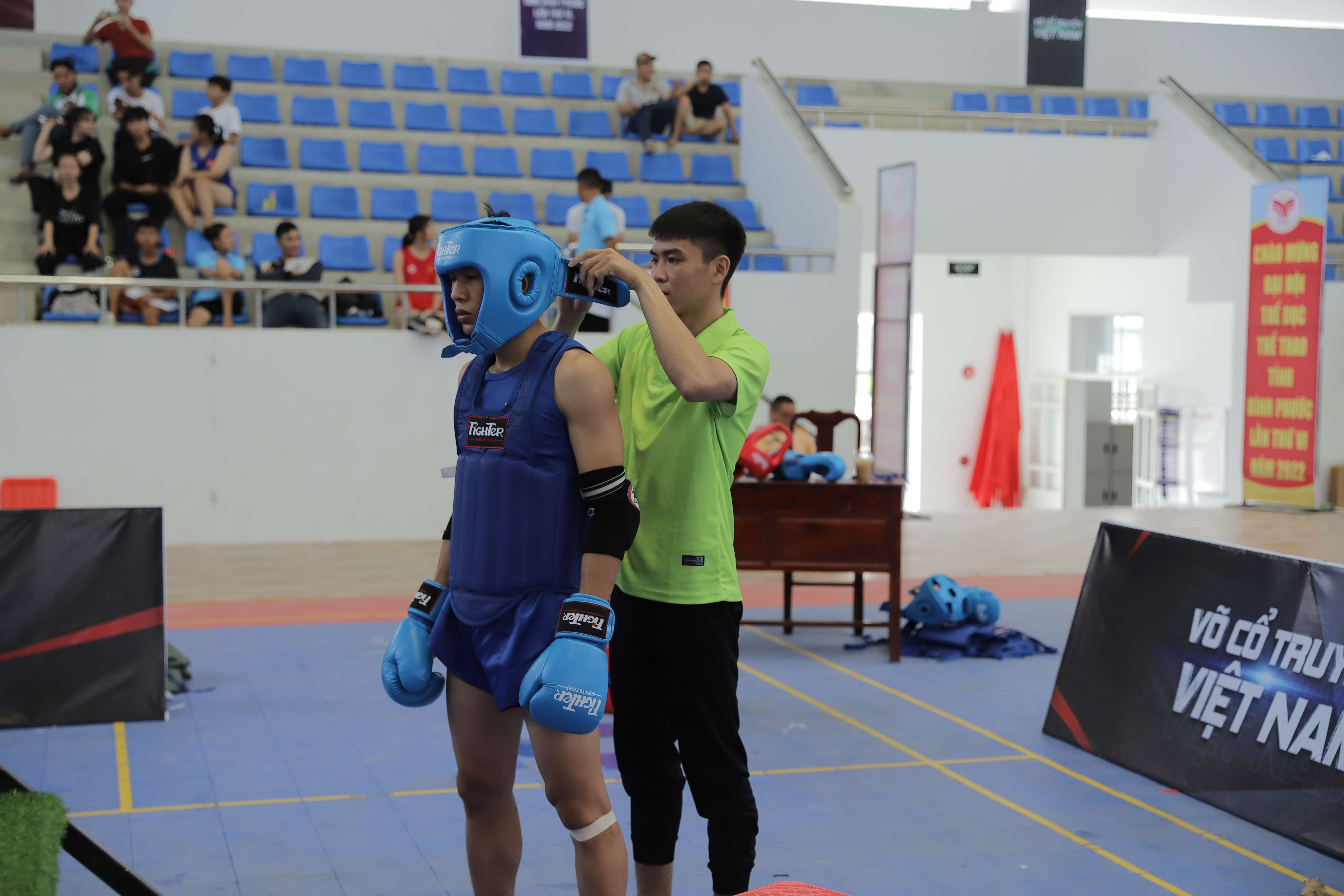 A martial arts fighter wearing protective gear prepares with a trainer by his side.