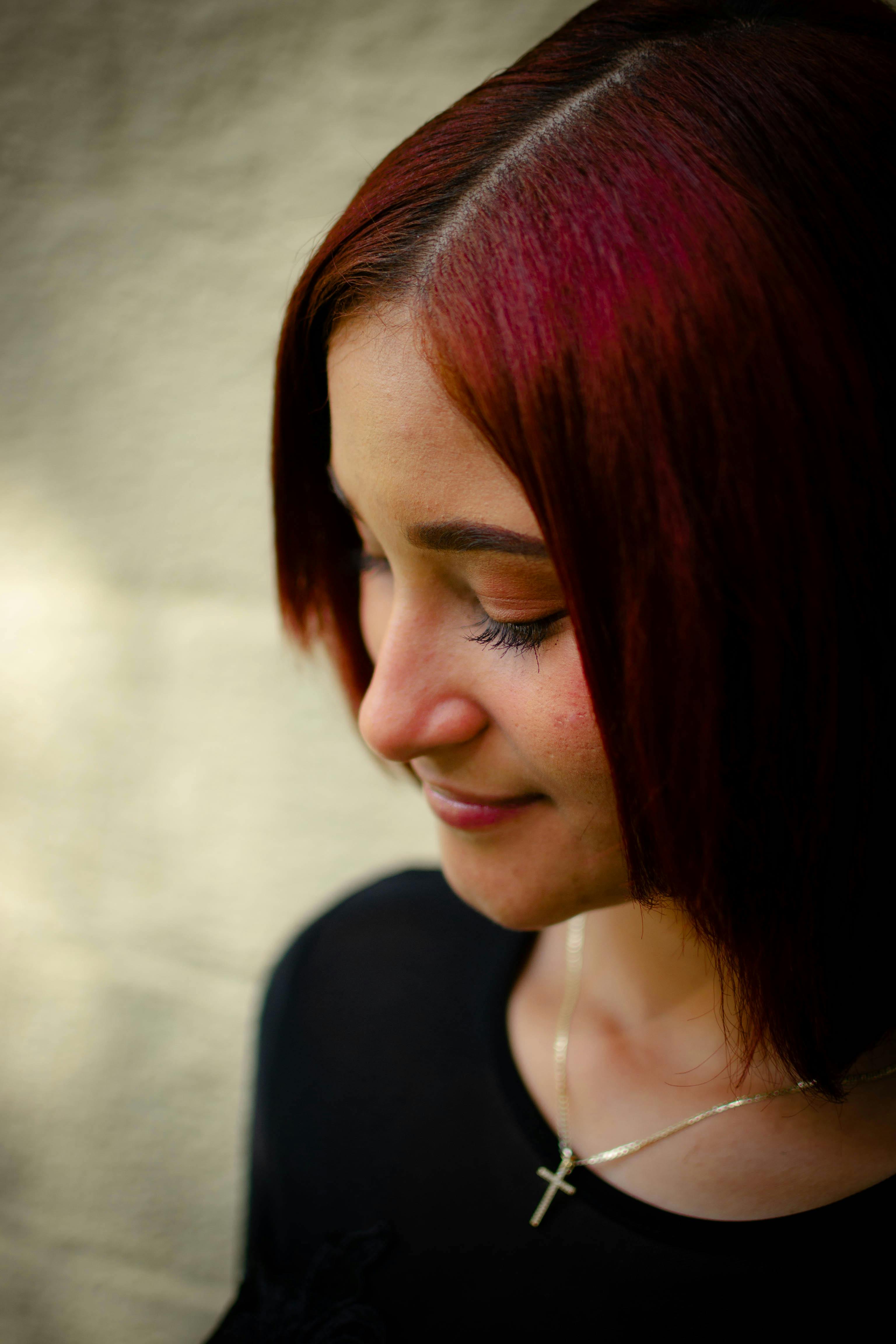 A serene portrait of a woman with red-dyed hair, smiling gently and wearing a cross necklace.