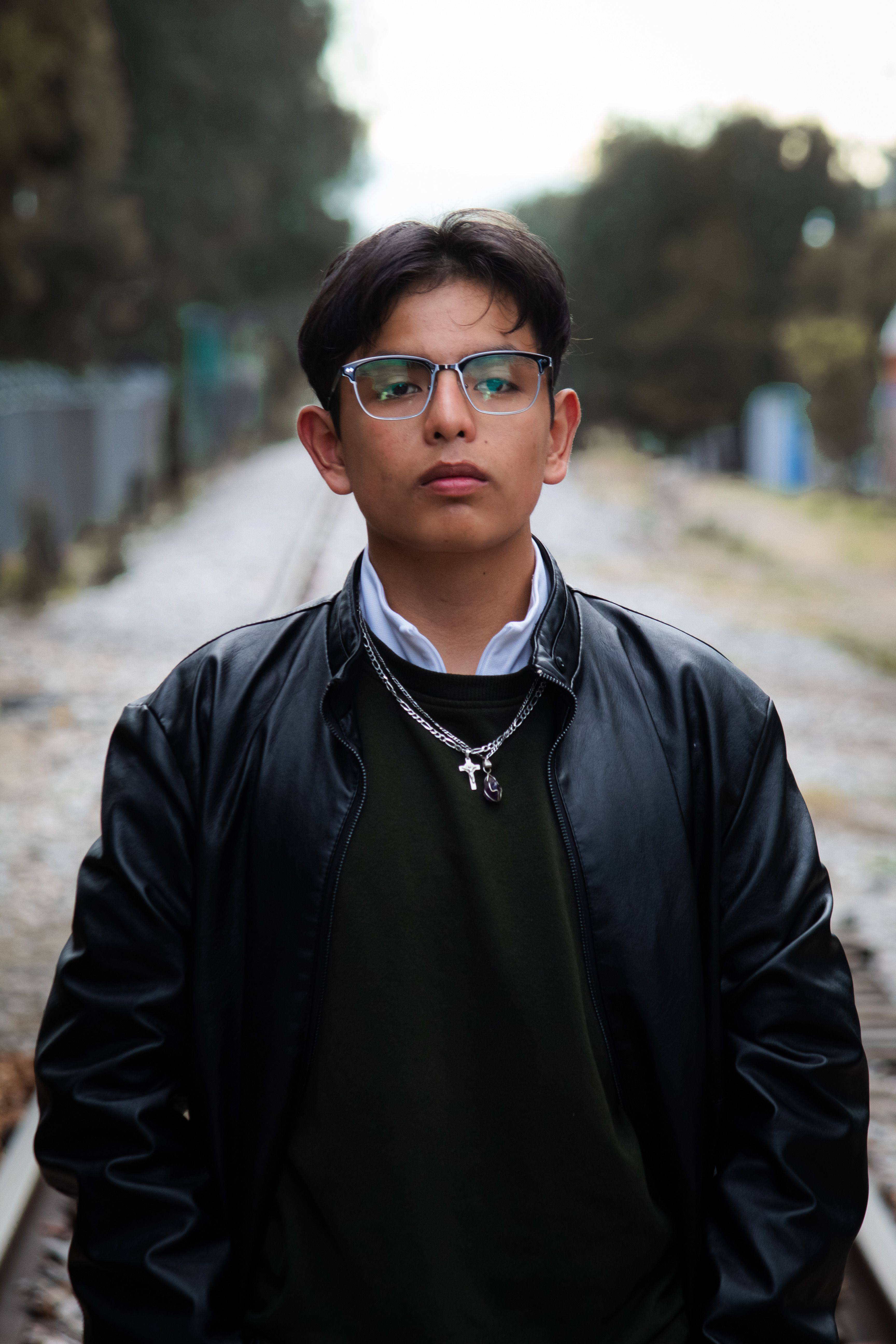 Portrait of a young man in a black leather jacket standing outdoors on a rail track.