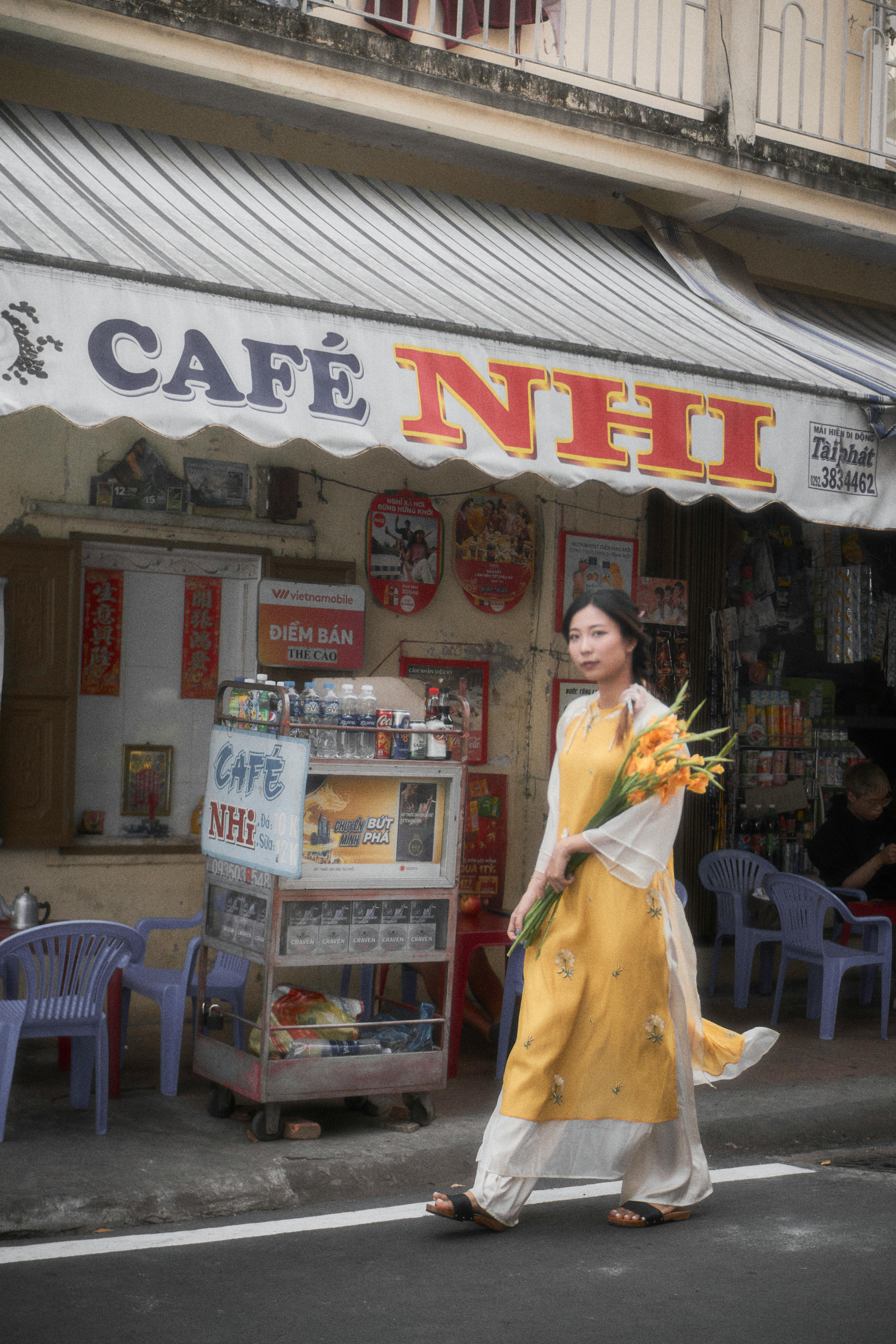 Woman in traditional yellow dress walking by a cafe in Can Tho, Vietnam.