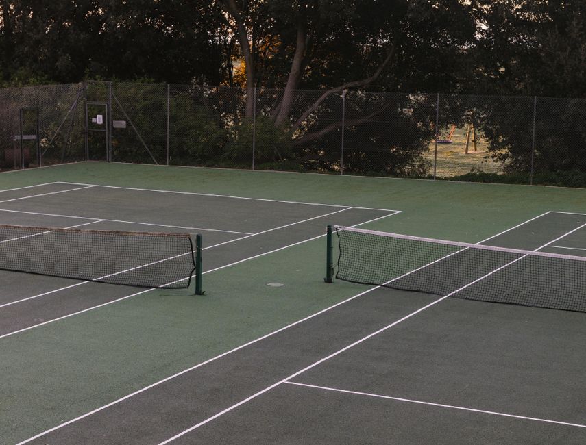 Empty outdoor tennis court surrounded by trees, perfect for sports enthusiasts.