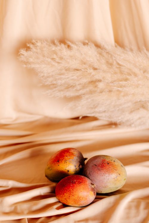 Free Artistic still life featuring three fresh mangoes with pampas grass on a beige background. Stock Photo