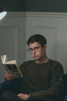 晚上，一个戴眼镜的年轻人在舒适的室内环境中看书