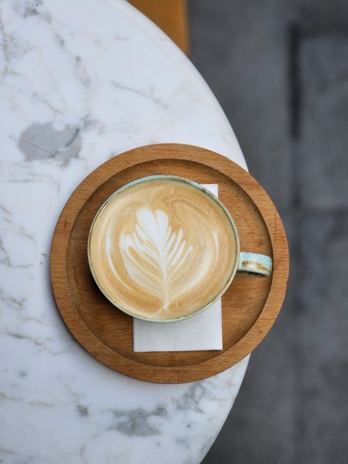 Free Top view of a cappuccino with frothy leaf art, placed on a wooden tray over a marble table. Stock Photo