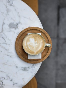 A top view of a cappuccino with latte art on a wooden tray, placed on a marble table.