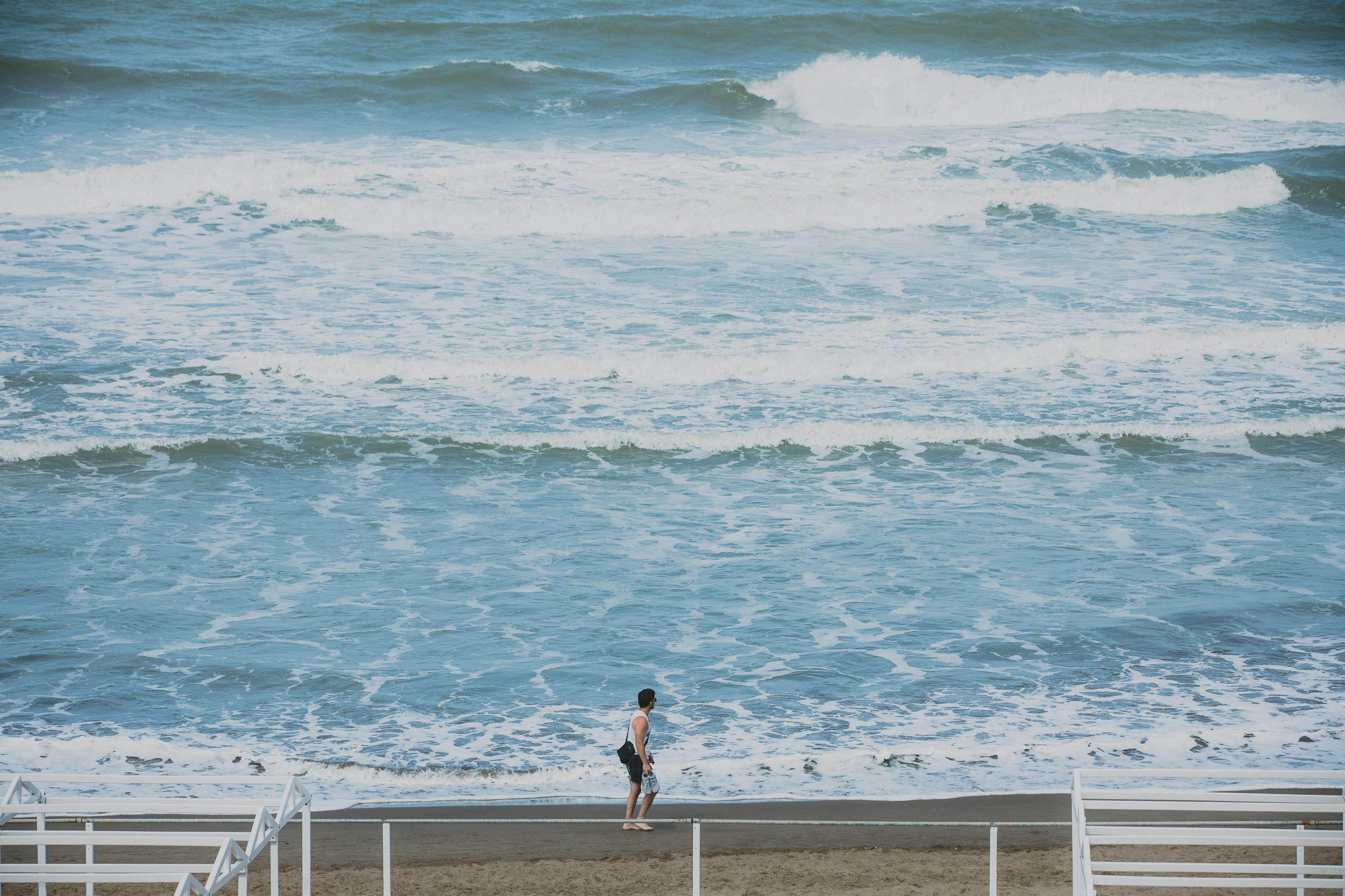 A lone man walks by the ocean waves on a tranquil beach day.