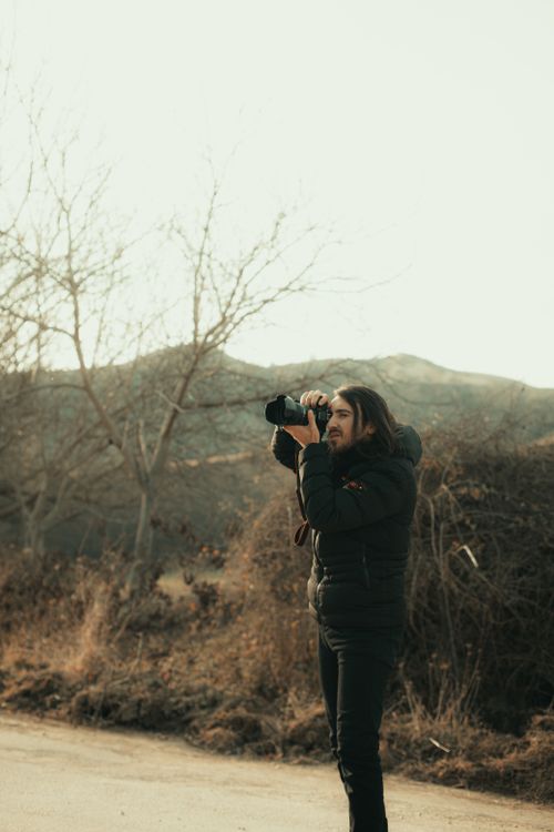 Free Man in a jacket taking photos in a rural setting with a Canon camera. Stock Photo