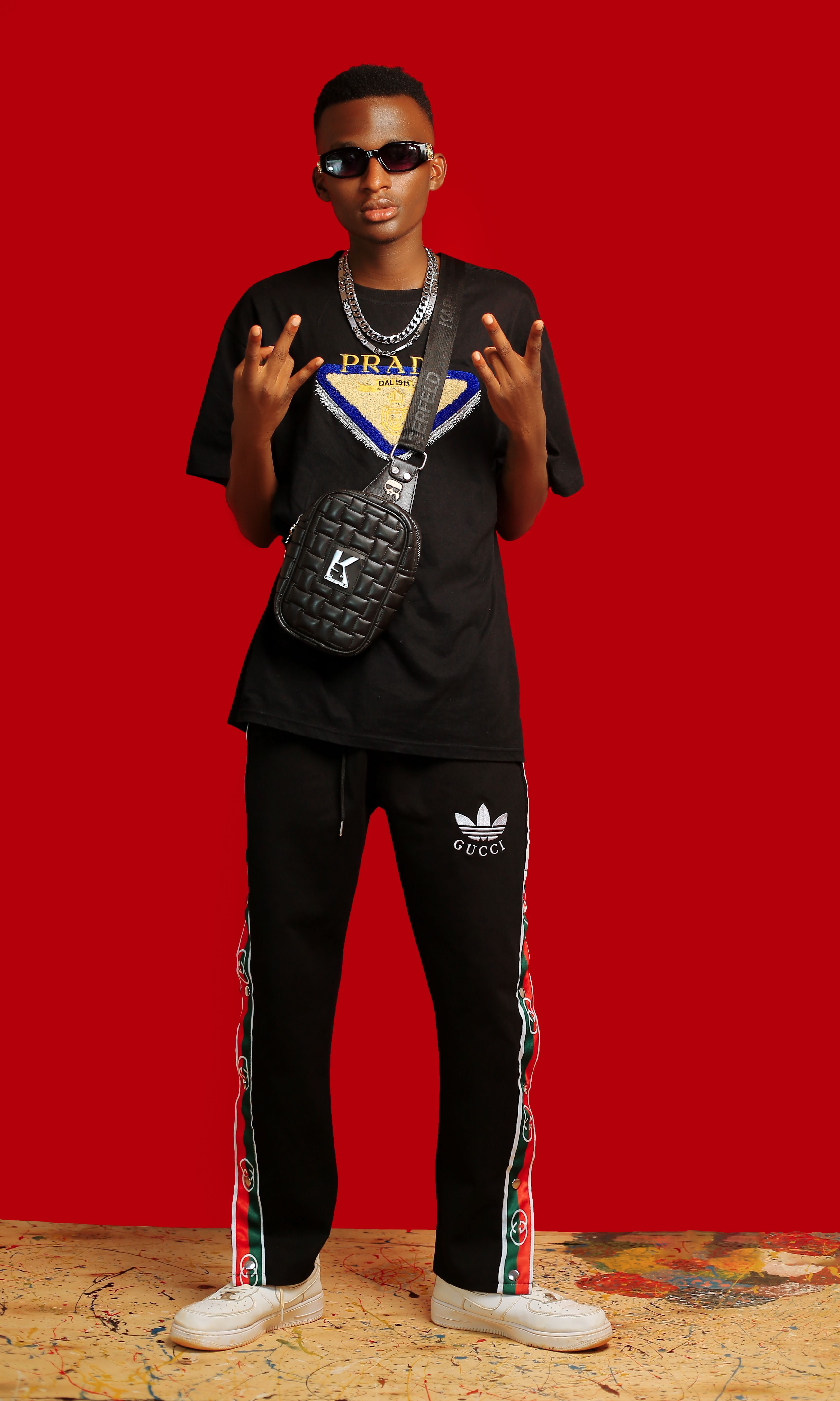 Streetwear fashion portrait with sunglasses and logos on bold red backdrop.