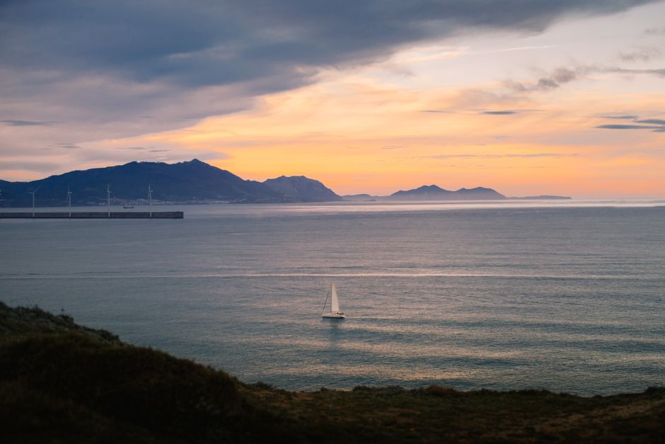 Scenic view of sailboat at sunset near Bilbao's coastline with mountains in the background.