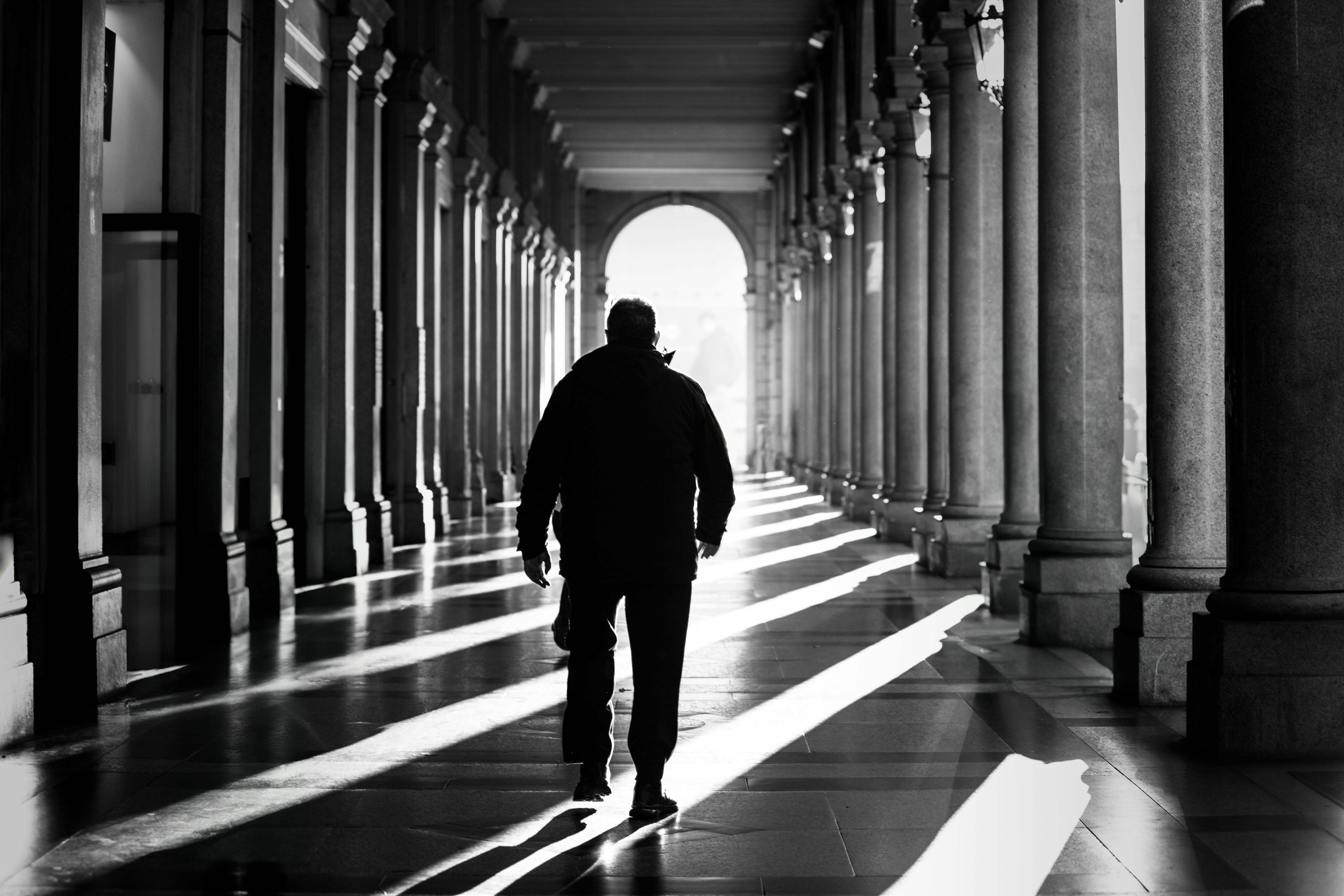 Silhouette of a man walking through a sunlit colonnade in Torino, Italy, captured in striking black and white.