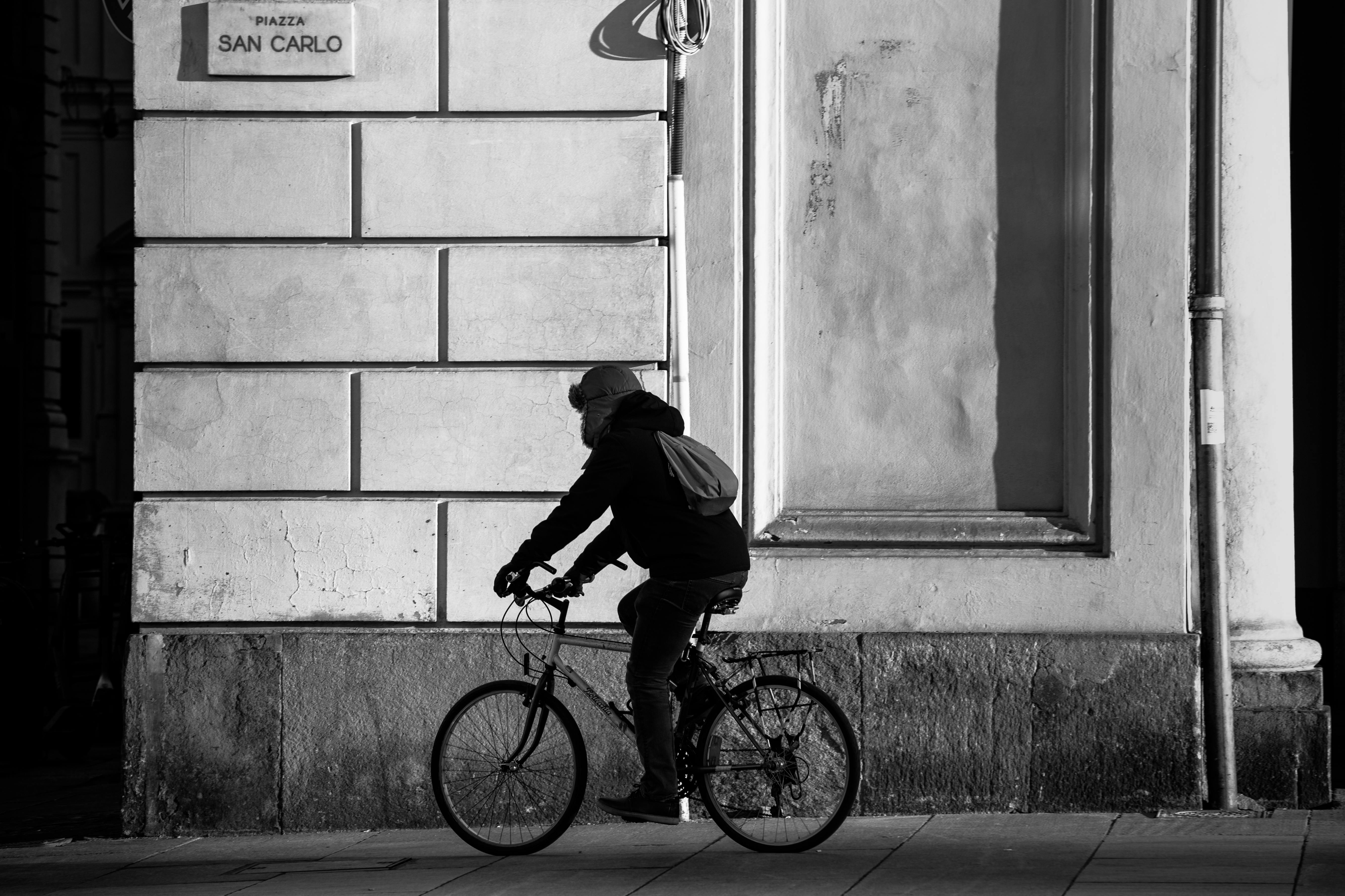 Una persona in bicicletta accanto a un muro storico in Piazza San Carlo, Torino, in una foto in bianco e nero.
