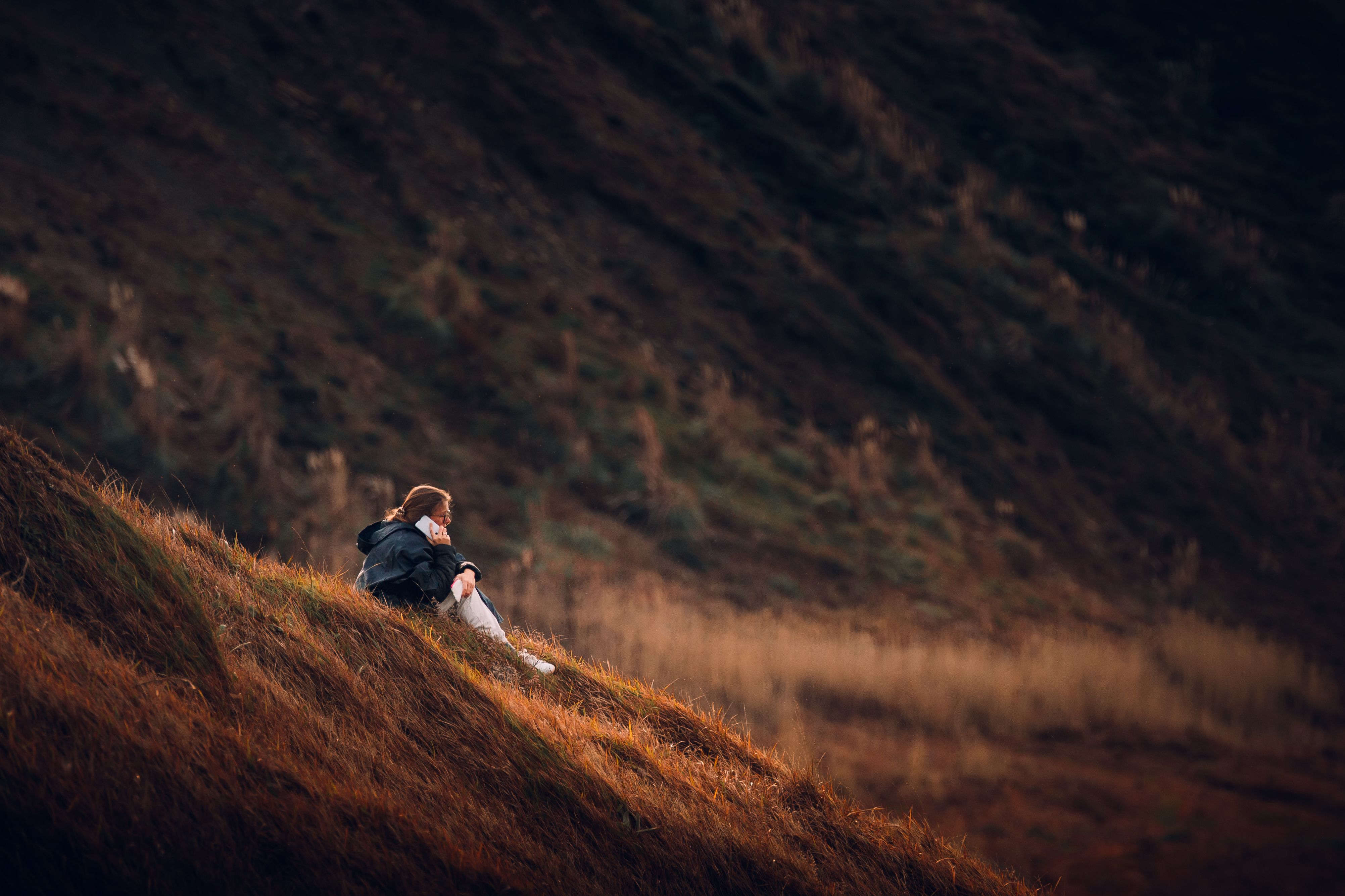 A woman enjoys a peaceful moment on a grassy hillside, surrounded by a tranquil landscape.