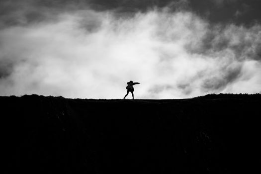 Artistic black and white silhouette of a woman standing on a hill against a dramatic cloudy sky in Bilbao.