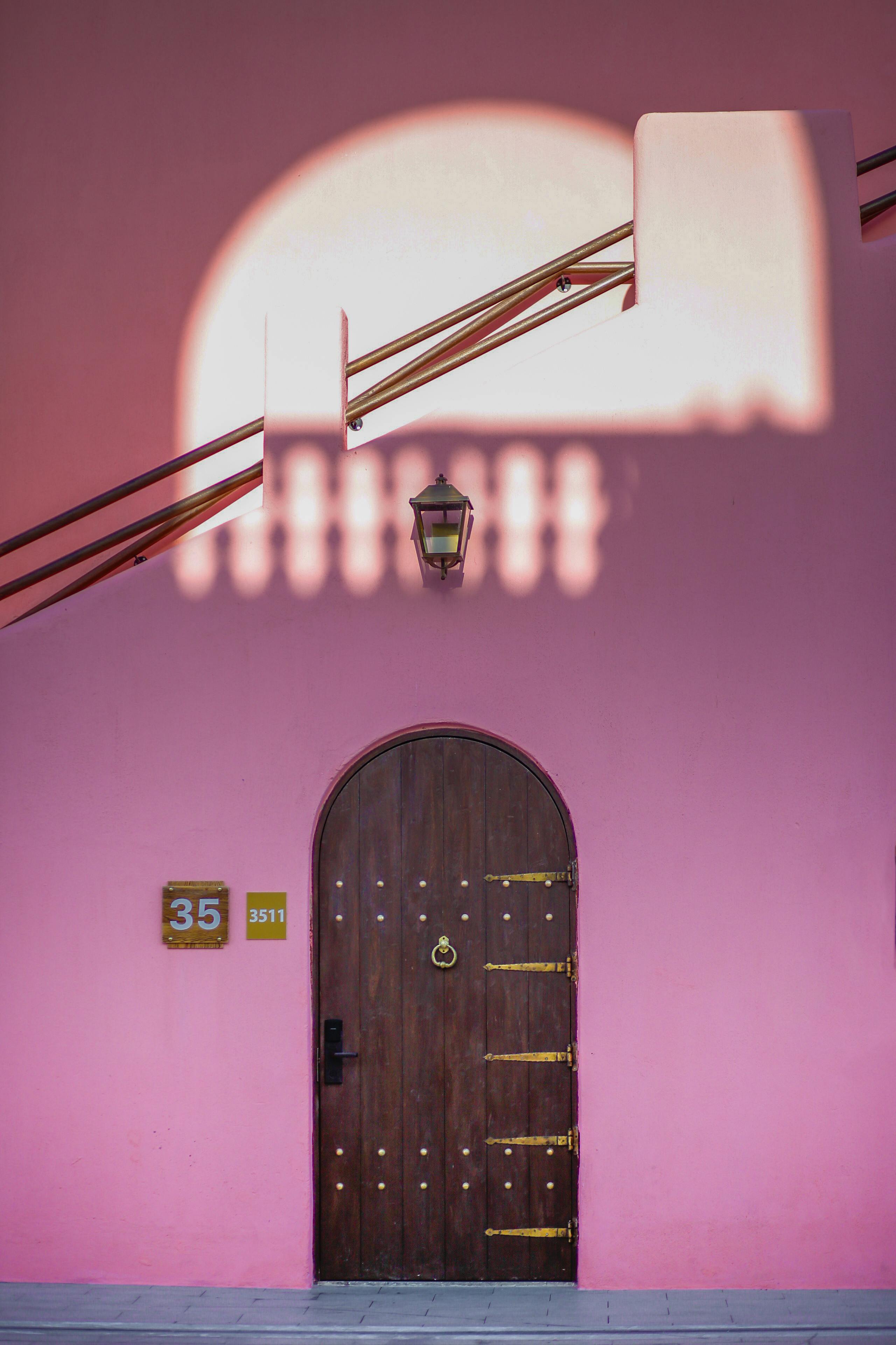 A captivating pink house facade with a wooden door and shadows in Doha, Qatar.