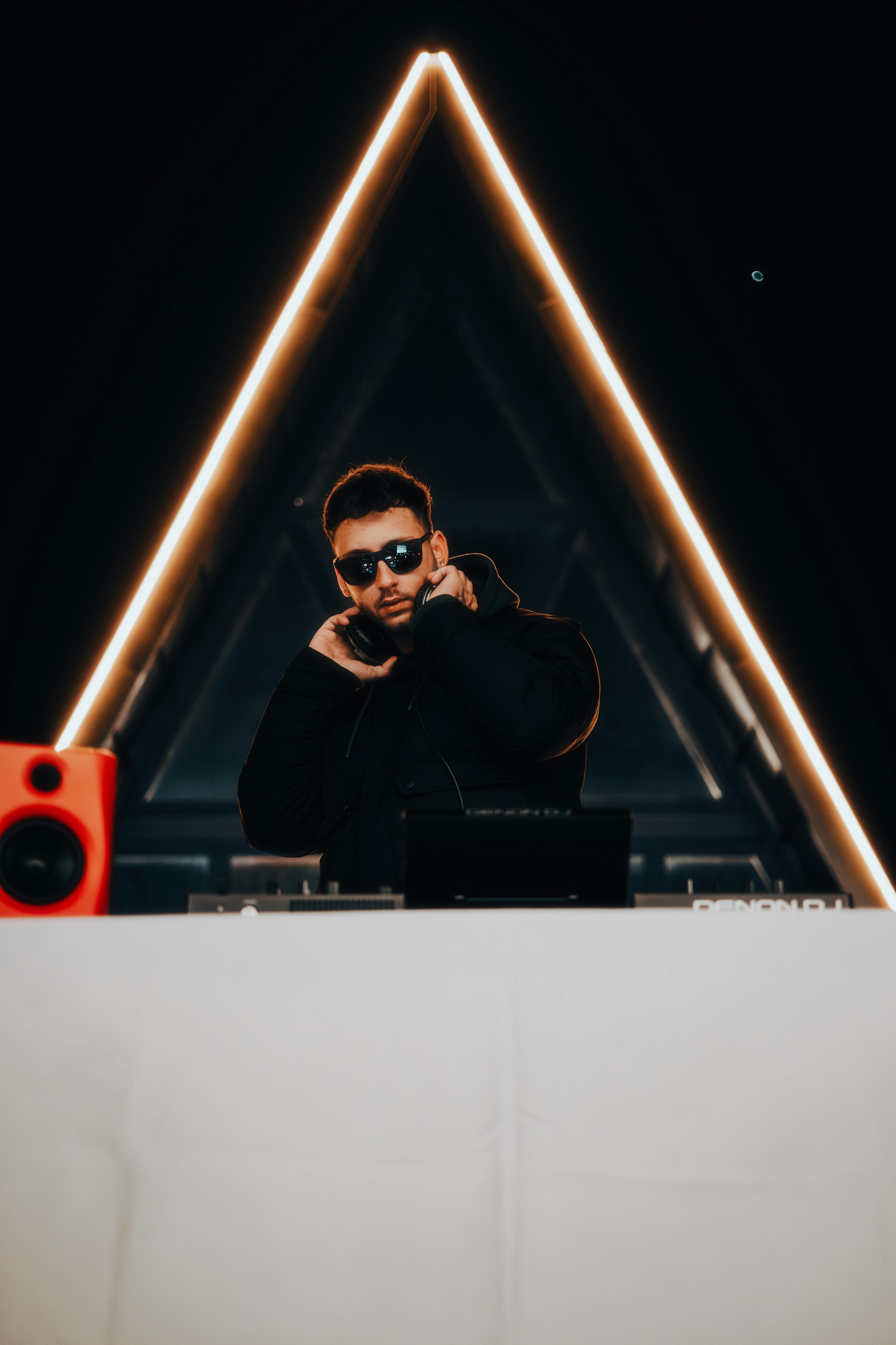 DJ with headphones performing live at a nightclub with illuminated stage design.
