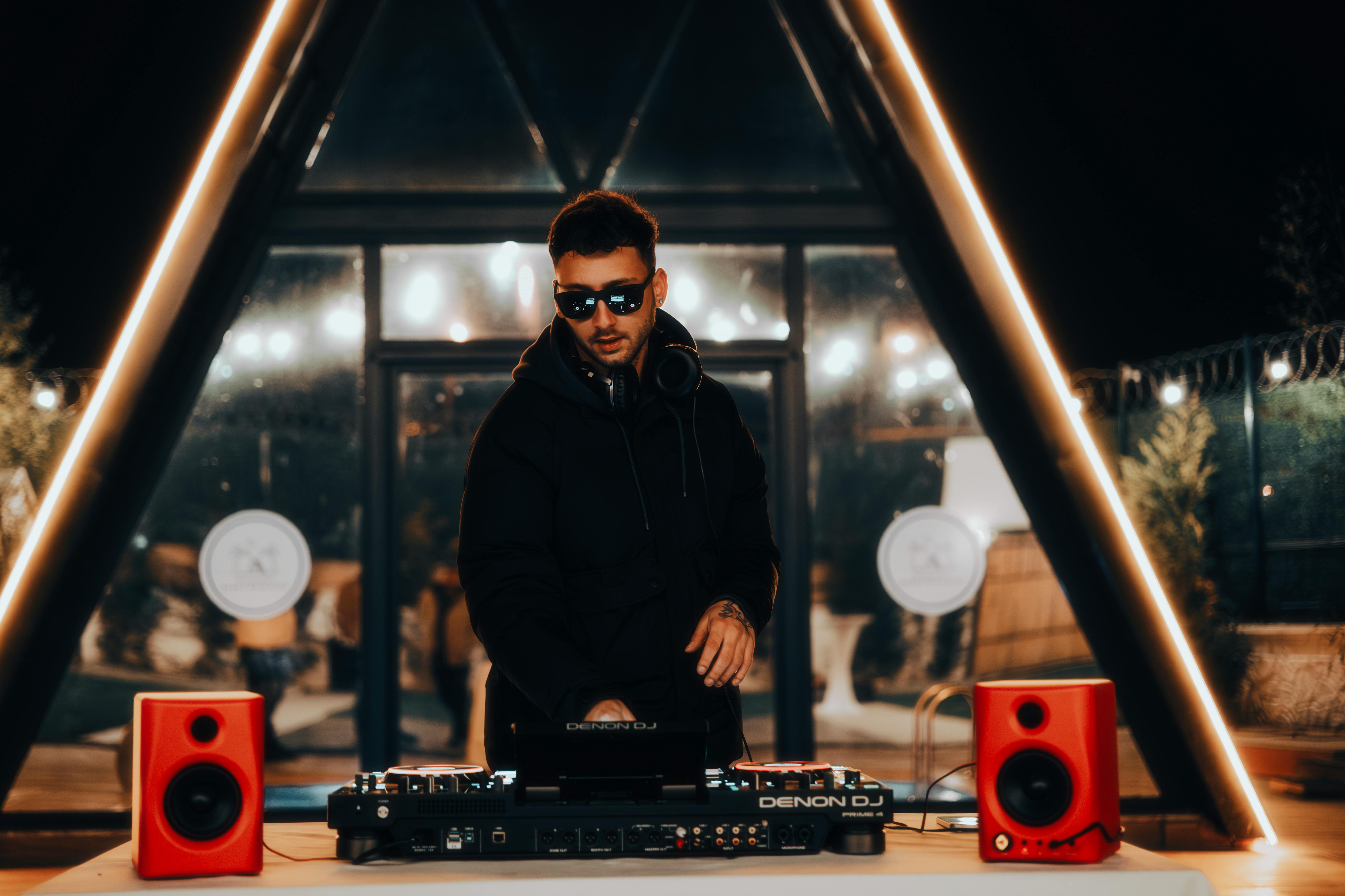 DJ mixing at night, surrounded by vibrant lights and audio equipment in a stylish venue.