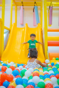 Happy children playing on slides and in a ball pit at an indoor playground.