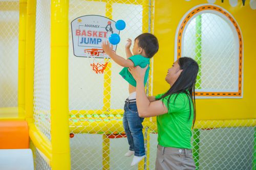 Free A joyful scene of a mother lifting her child playing with blue balloons at an indoor playground. Stock Photo