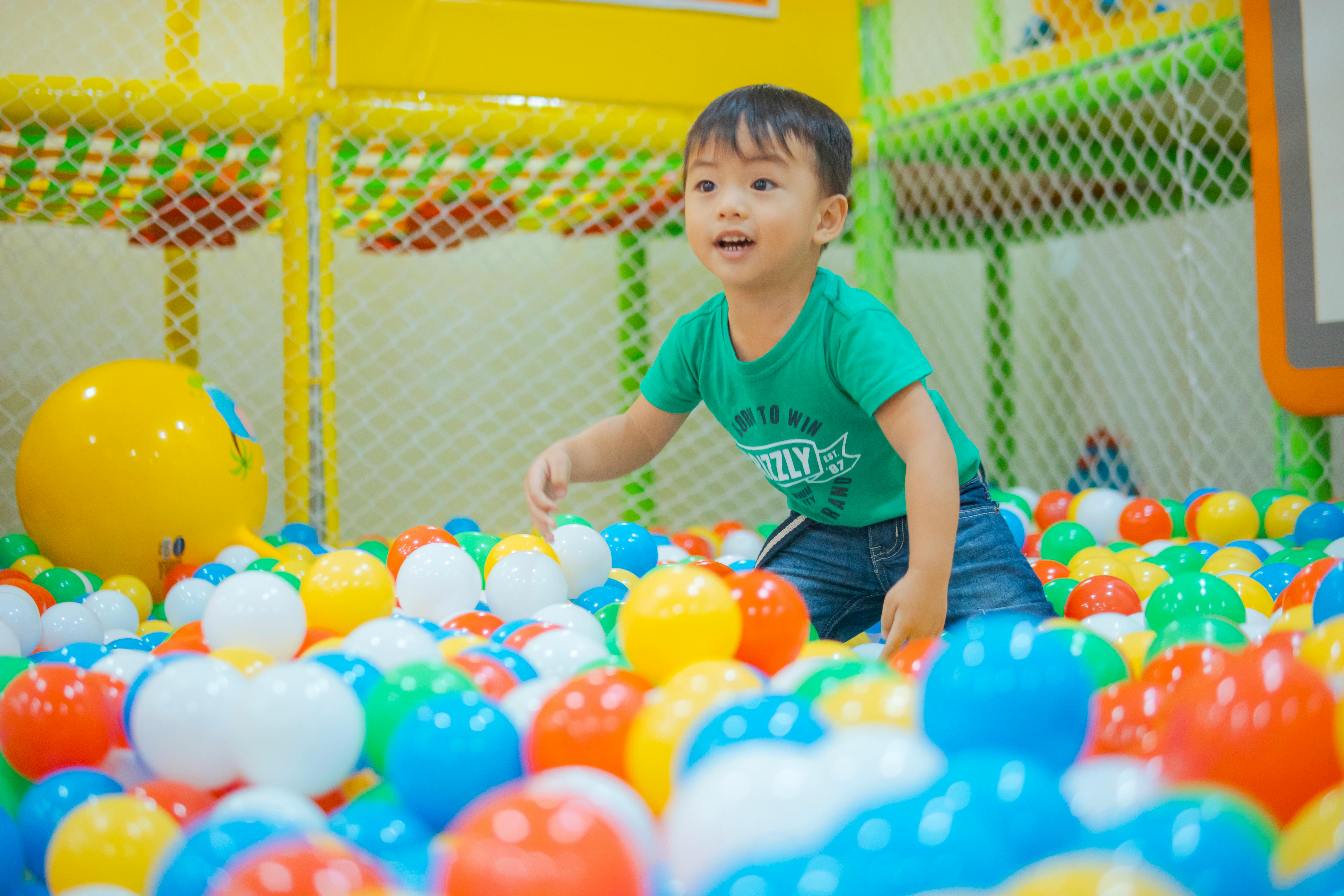 A young child having fun in a vibrant indoor ball pit, filled with colorful plastic balls.