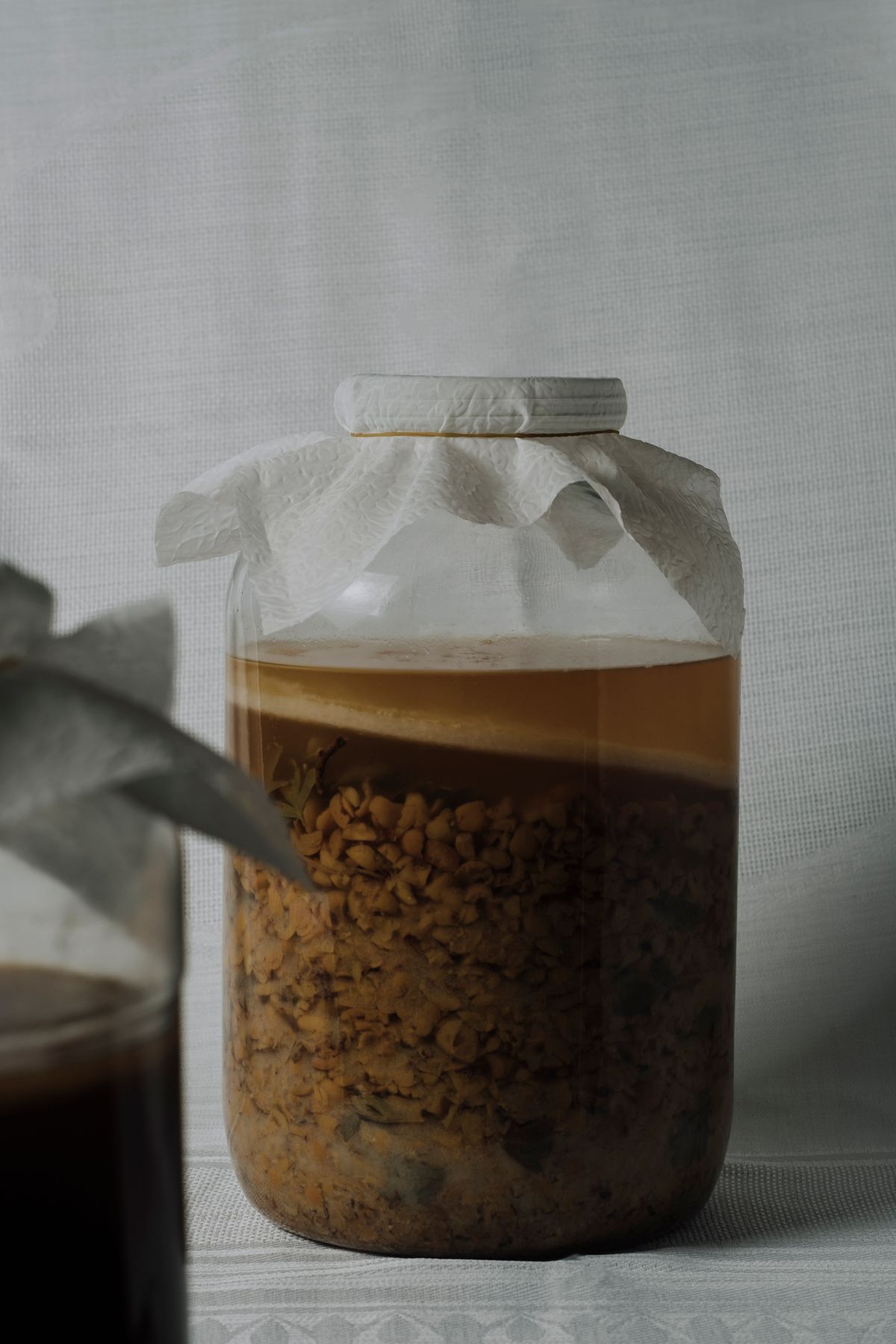 A sealed glass fermentation jar with a handwritten label showing a vegetable ferment in progress