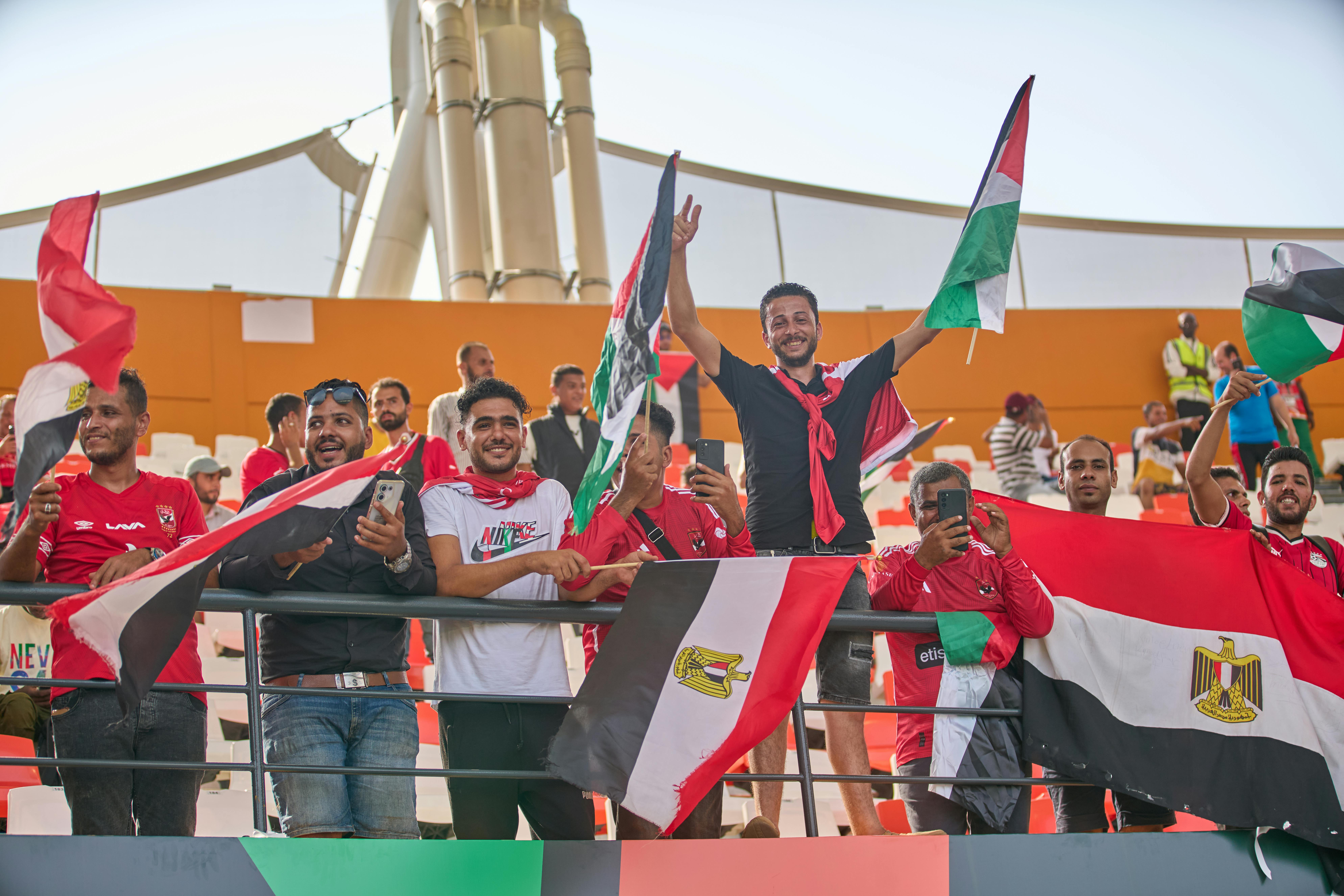 Group of enthusiastic soccer fans holding flags and cheering at a stadium event.