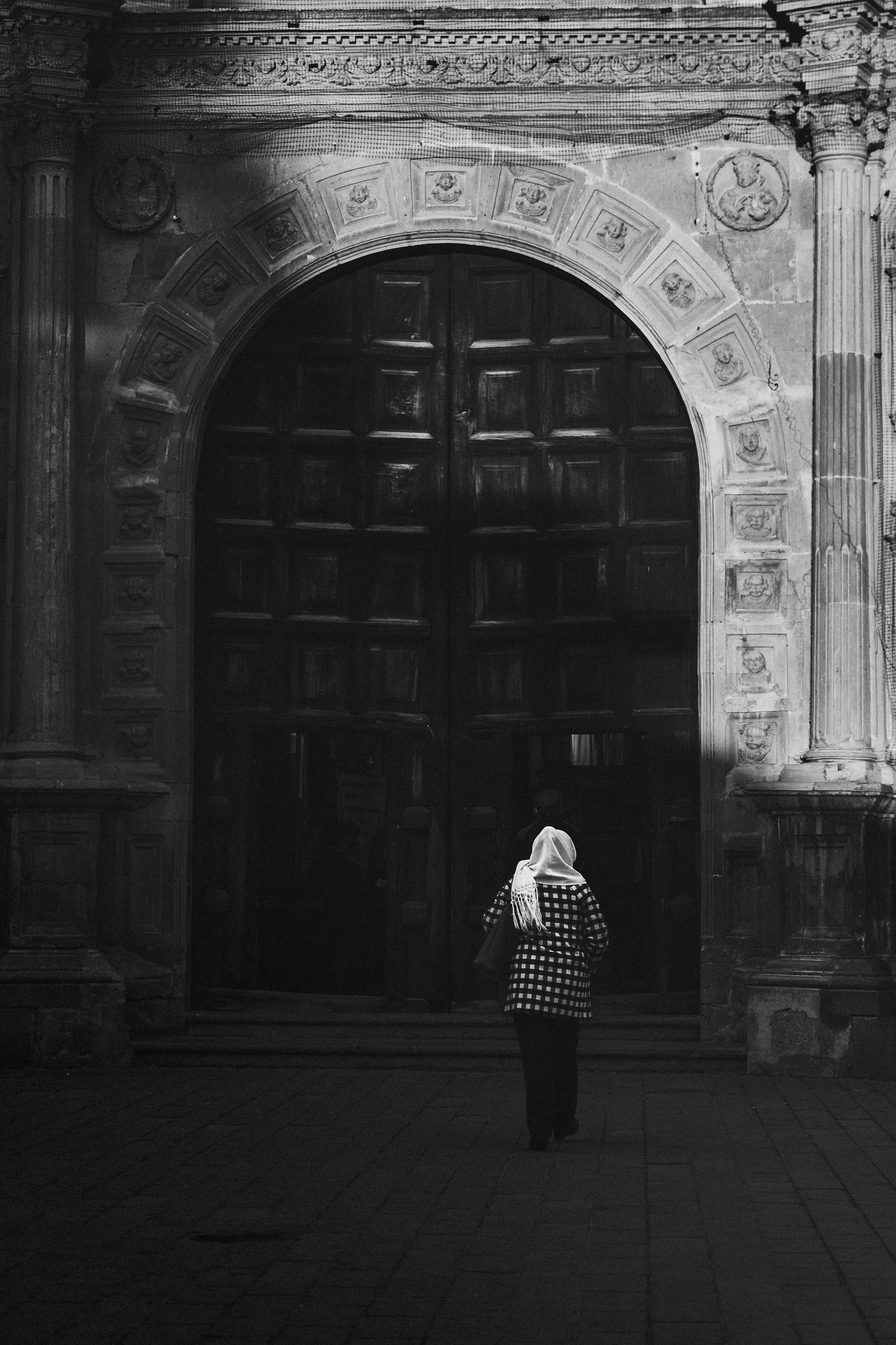 A person in a hijab approaches a monumental door in Actopan, Mexico.