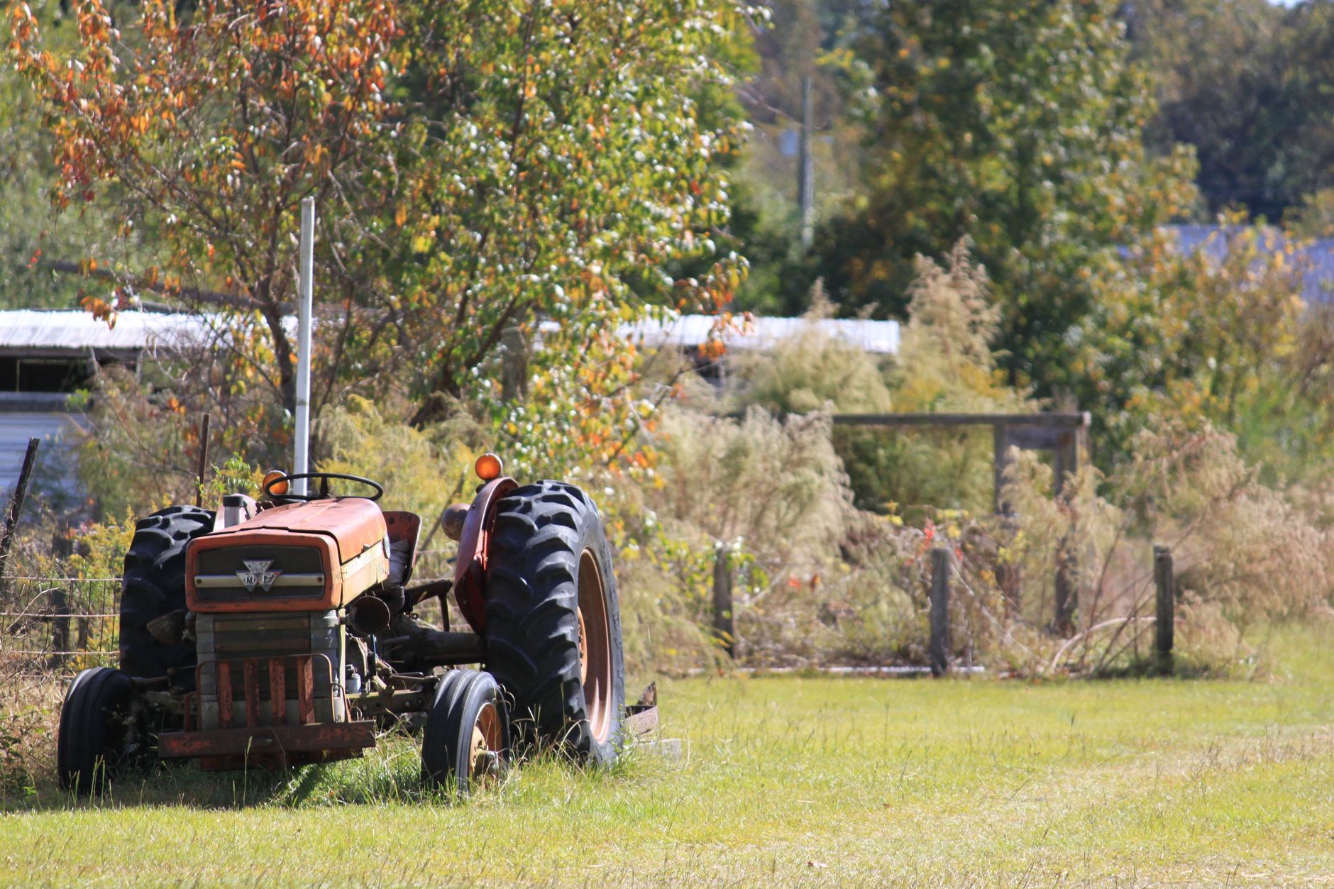 A vintage tractor rests in a verdant rural landscape with trees and grass.