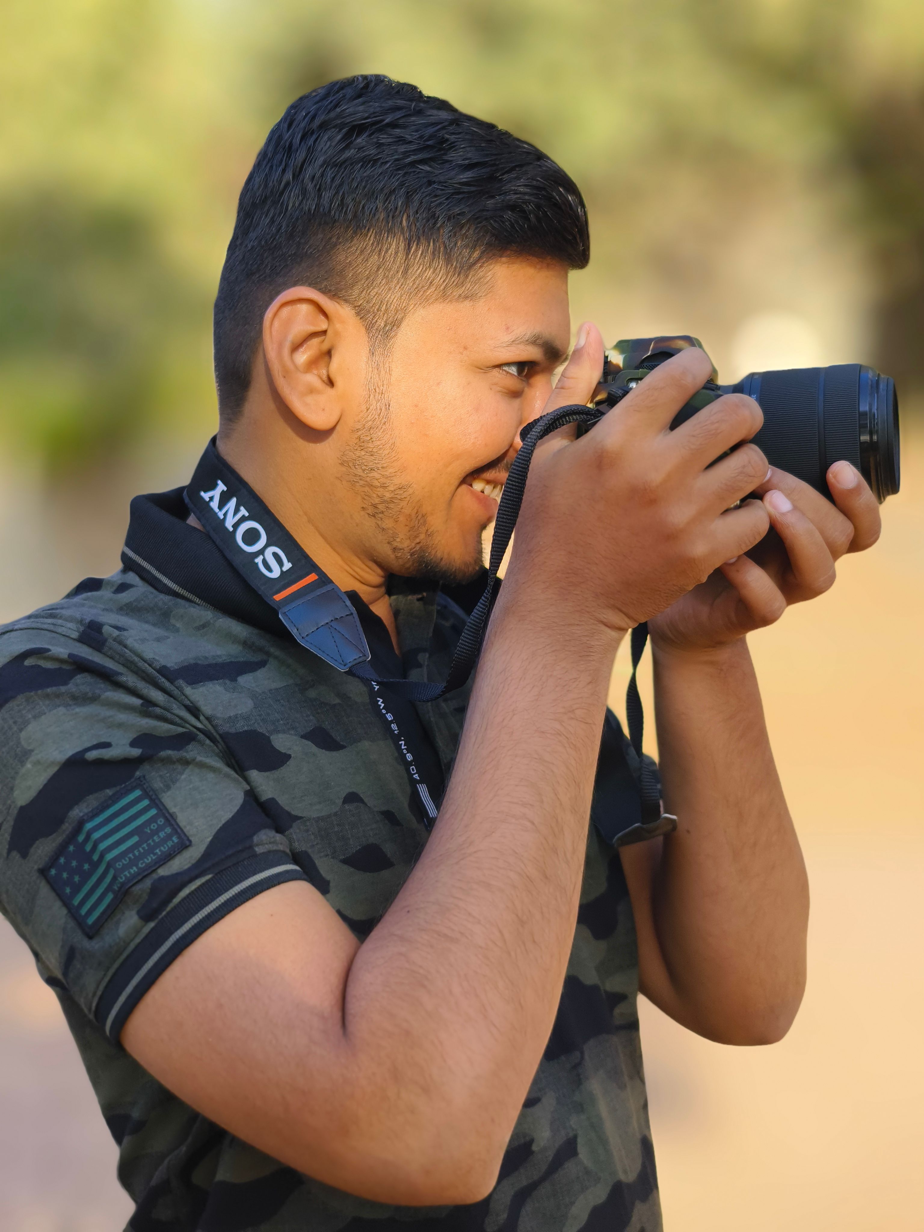 Smiling young man with camera capturing photos outdoors during the day.