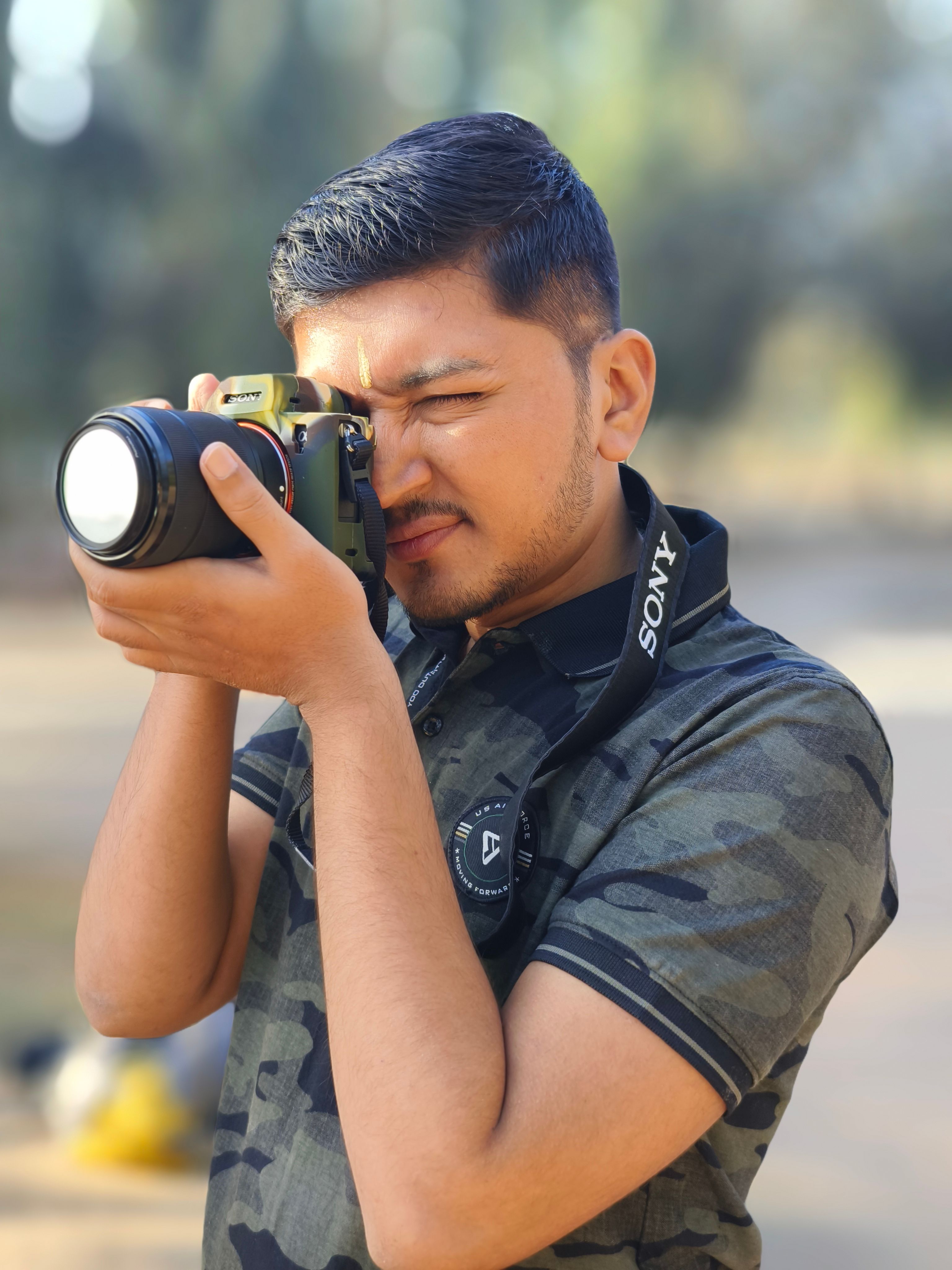 Adult man using a camera with focus and concentration in a sunny outdoor environment.