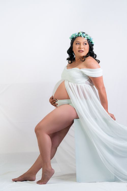 Free Beautiful pregnant woman in flowing white dress posing gracefully indoors. Stock Photo