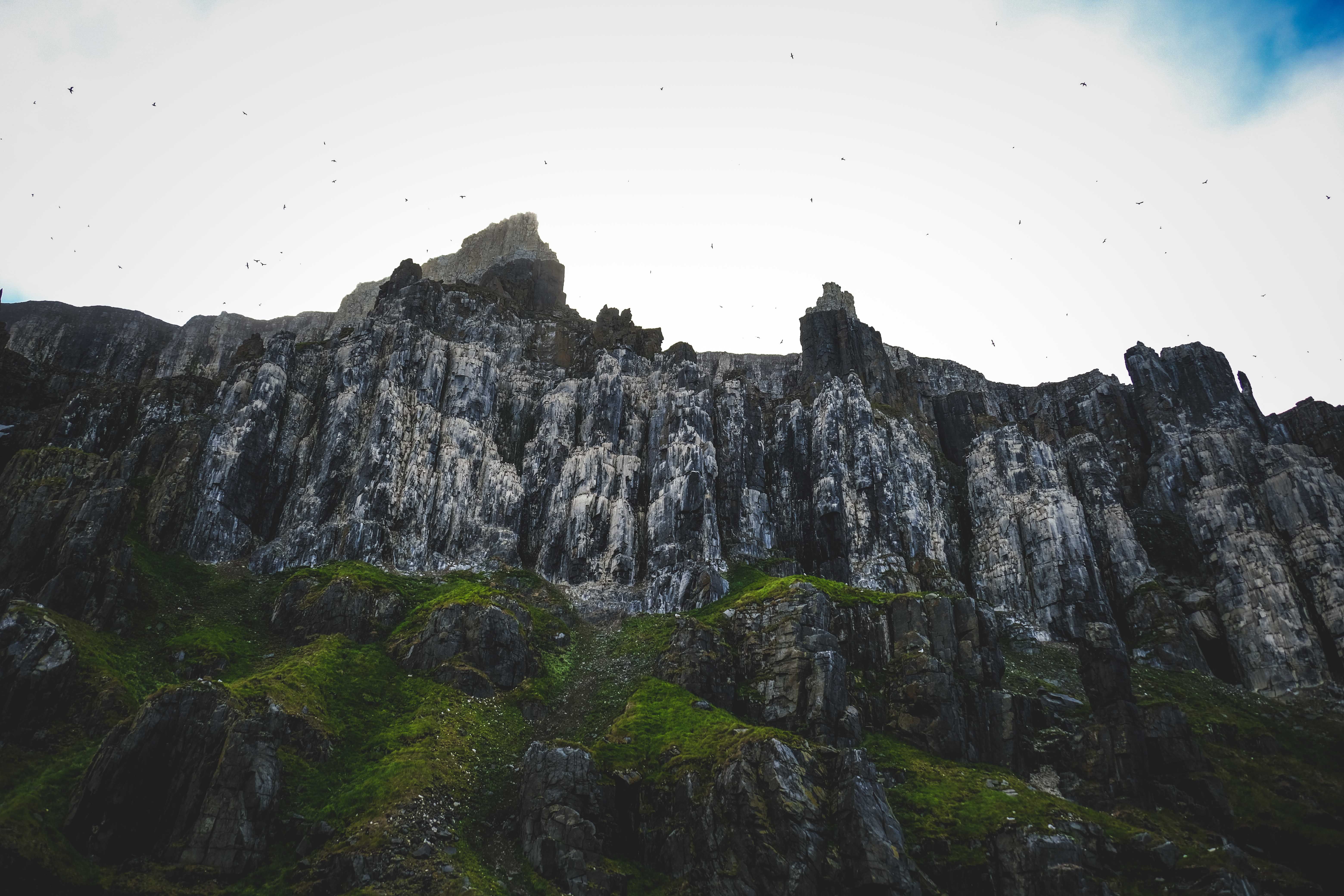 Dramatic cliff landscape with eroded rocks and lush greenery under an overcast sky.