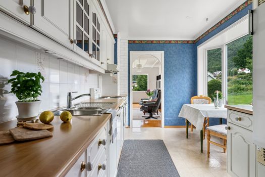 Spacious white kitchen with blue walls and natural light, featuring a dining area.