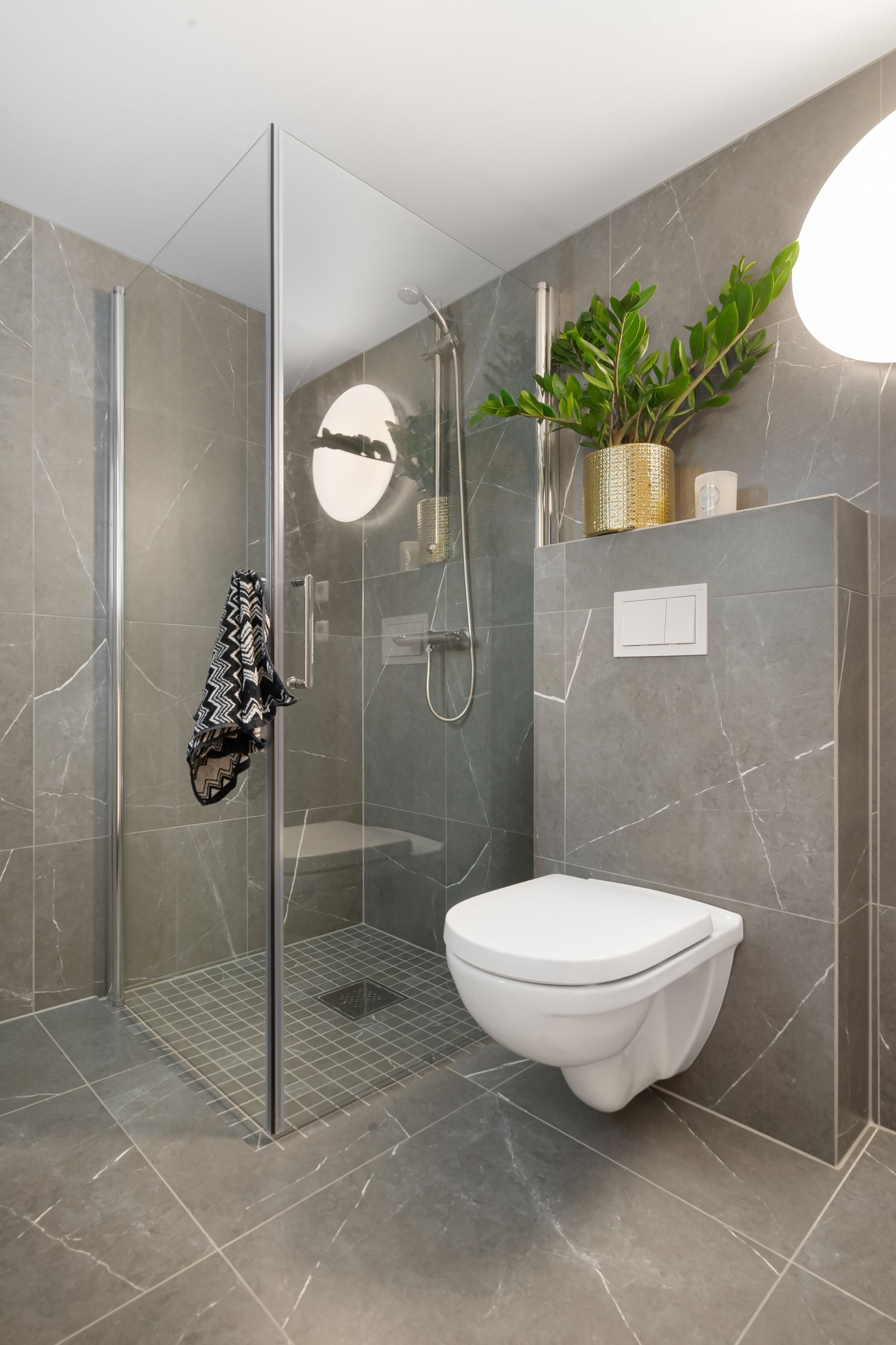 Grey tiled bathroom with glass shower, toilet and small plant