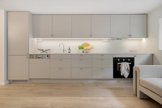 Bright modern kitchen interior featuring sleek white cabinets and wooden flooring.