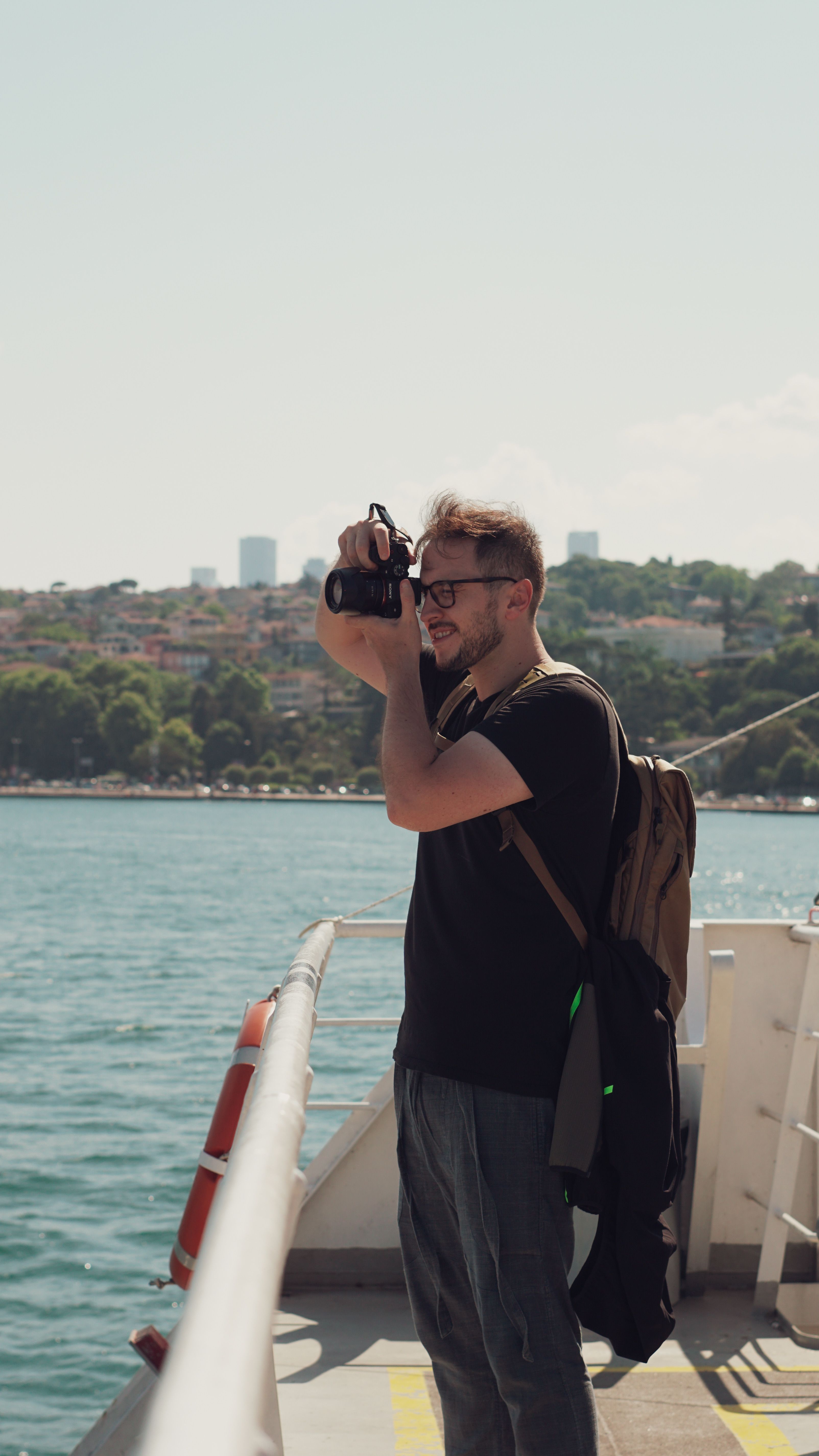 Man taking photos on a ferry with a scenic seaside cityscape in the background.