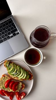 Top view of avocado toast and tea alongside a laptop in a minimalist setting, perfect for breakfast inspiration.