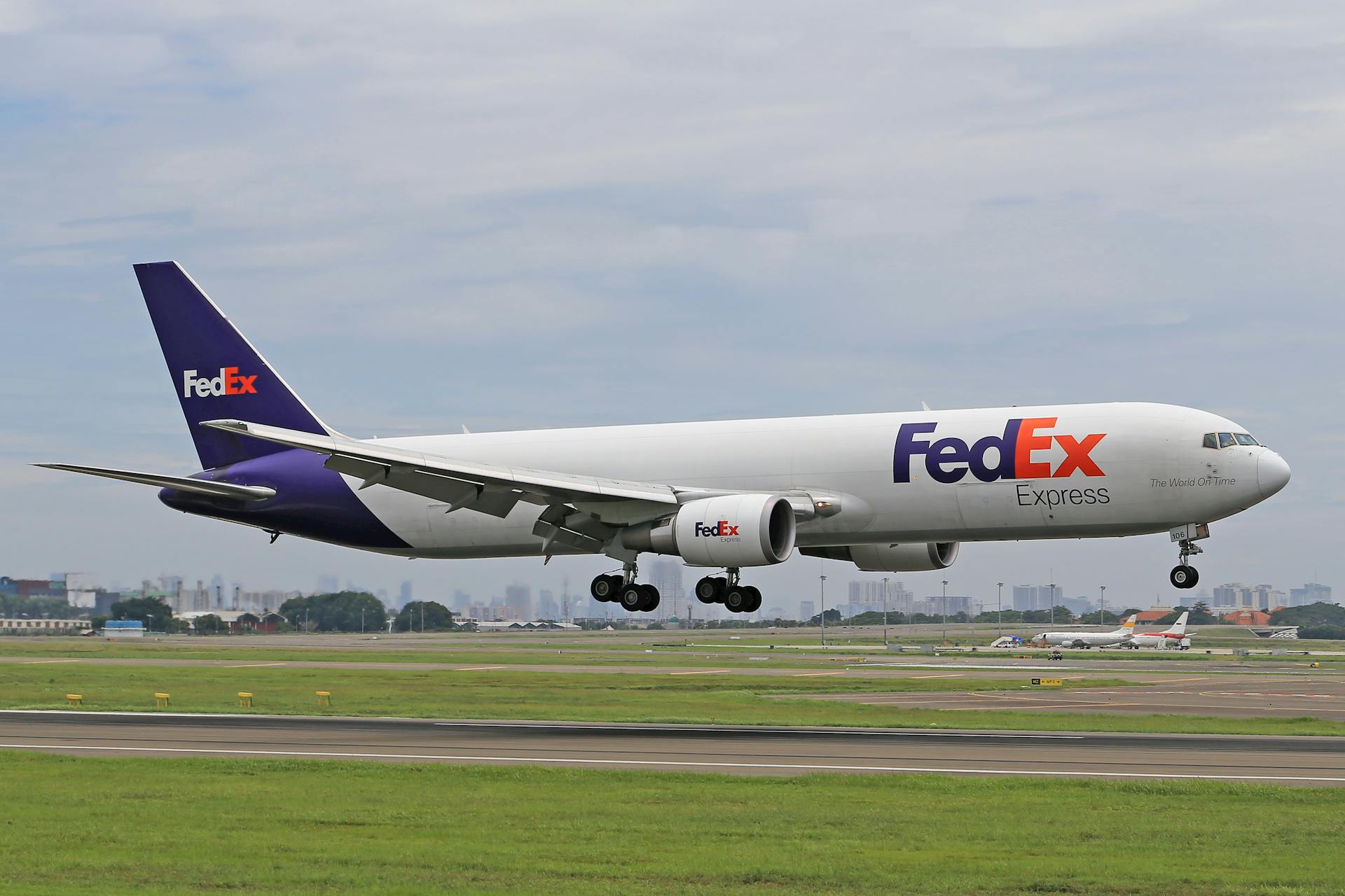 FedEx cargo airplane approaching runway for landing at a busy airport.