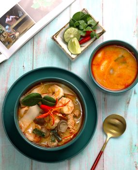 Flat lay of Burmese shrimp soup with lime, chili, and vegetables on a turquoise table.