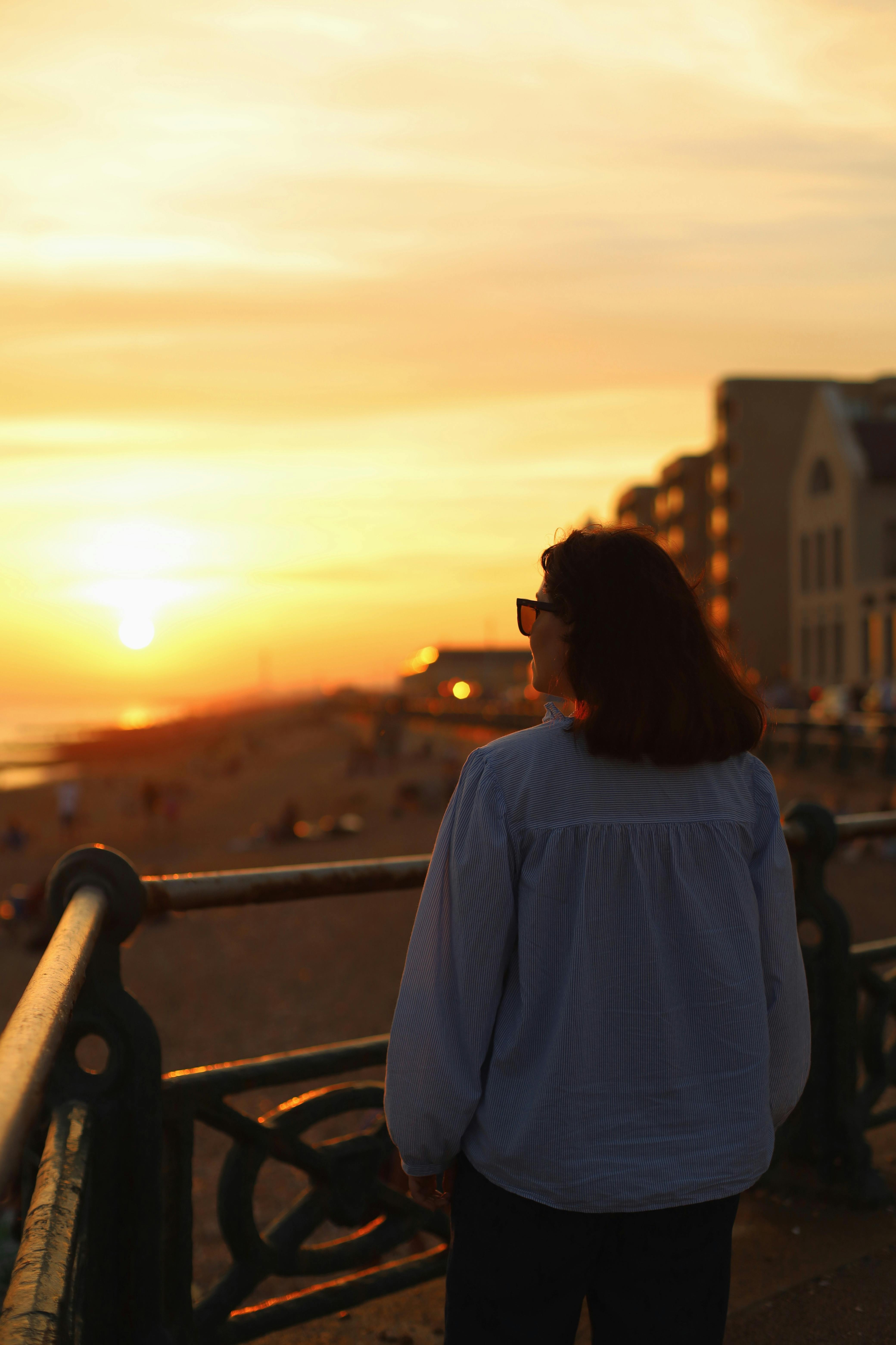 A woman standing on a balcony enjoys a beautiful sunset at a beach in England.