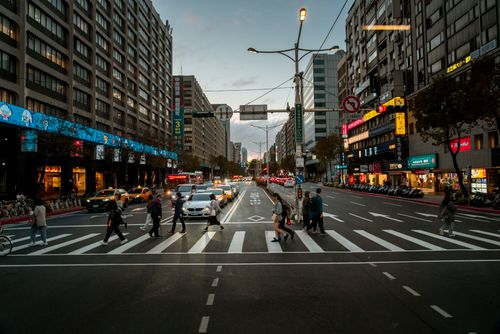 Free City street view of pedestrians crossing at dusk, showcasing modern urban life and architecture. Stock Photo