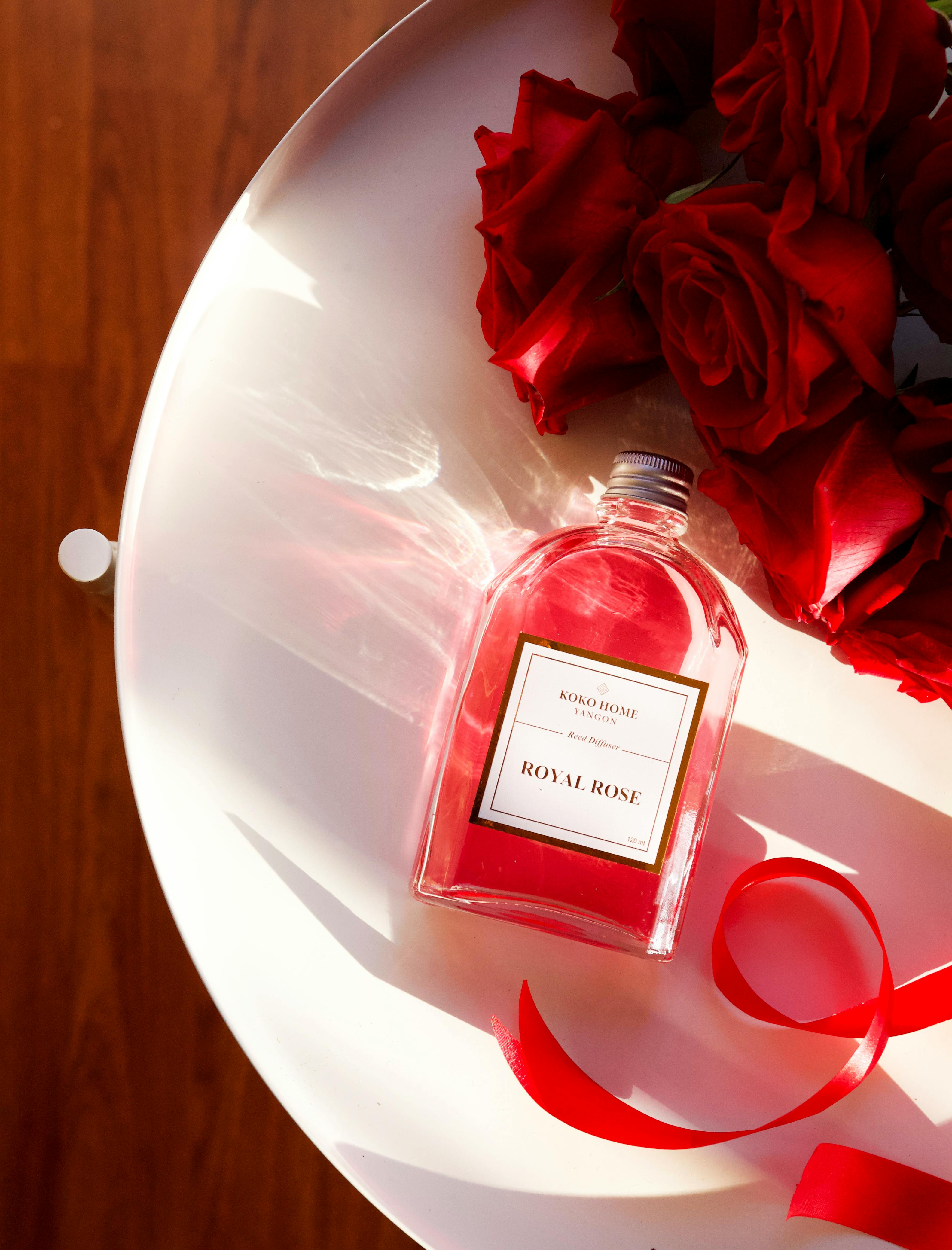 Luxurious perfume bottle with red roses on a white surface, illuminated by sunlight.