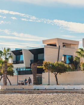 Contemporary seaside home with palm trees and a sandy beach in the foreground.